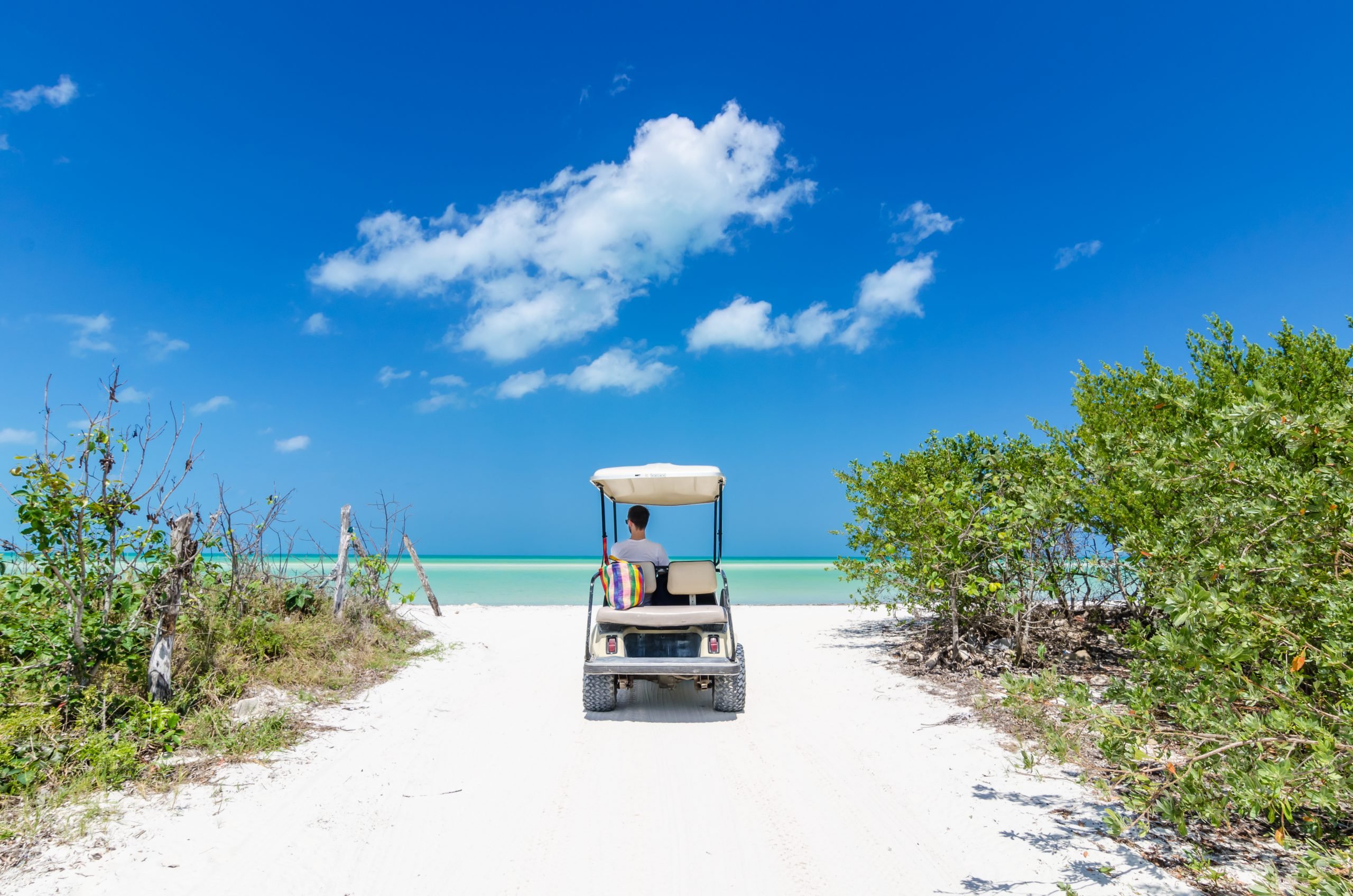 Young man driving on golf cart at tropical sandy beach